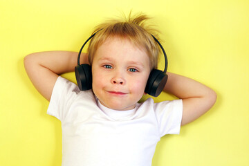 Cute little child boy listening to music with headphones on yellow background top view 