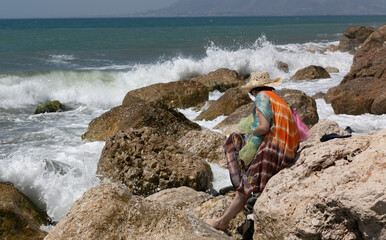 En la playa jugando con pañuelos de colores, una mujer vista de de atrás con sombrero de paja 