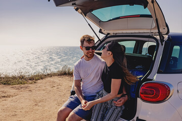 Happy young couple sitting on the trunk of the car