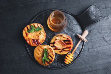 Delicious grilled peaches with honey and mint on black table, top view