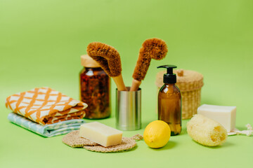 Zero waste, eco friendly home concept.Kitchen towels, bamboo brush, lemon, spray bottle, dark glass bottle, washcloth, wicker basket, shower sponge, soap on green background.