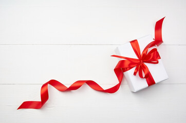 White gift box with red satin ribbon with bow on wooden background
