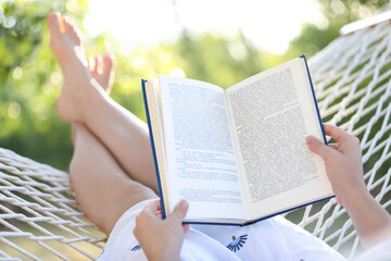 Young woman reading book in comfortable hammock at green garden, closeup - obrazy, fototapety, plakaty