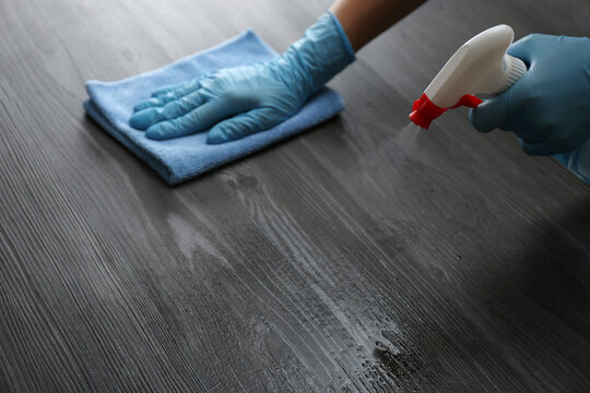 Woman in gloves cleaning black wooden table with rag and detergent indoors, closeup