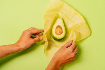 Organic fabric covers for food storage. Unrecognizable woman's hands holds reusable Beeswax Food Wraps with half of avocado.