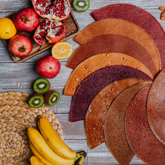 Many colorful fruit leathers with fresh fruits on the wooden table. Round fruit leather. Healthy food. Apples, bananas, nuts, lime, kiwifruits, pomegranate top view.
