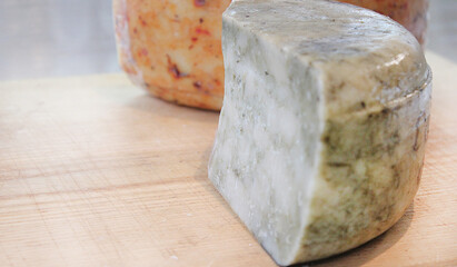 Farmer's cheese crust of cheese with grains inside. the texture as it Matures is handmade. pieces of cheese on a cutting Board in different colors of Derby, caciotta, cheddar