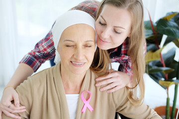 Smiling Caucasian Elderly Mother in white headscarf is sitting on wheelchair and hugging with daughter for love after chemotherapy. Senior woman is suffering from cancer or Leukemia patient.