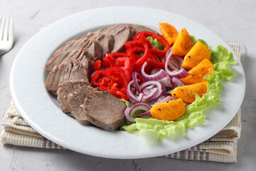 Sliced pork tongue with vegetables on white plate on grey background. Great cold appetizer.