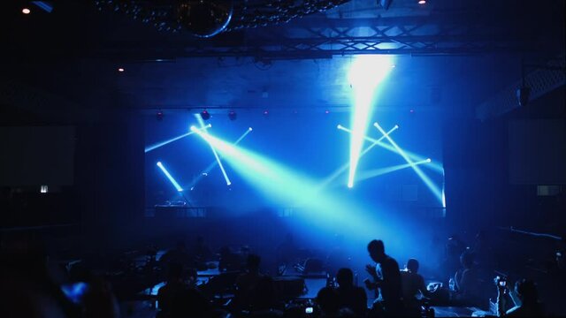 Illuminated Empty Blue Concert Stage With Fog And Rays Of Light In The Nightclubs. Musical And Dance Concept. Lights Beams On Stage With Musical Instruments. More People On The Ground Waiting Show