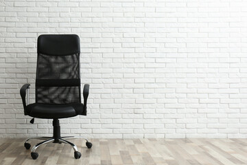 Comfortable office chair near white brick wall indoors. Space for text