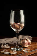 head of garlic with single garlic cloves on a wooden board and garlic in a glass goblet