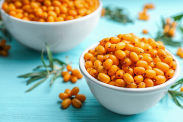 Fresh ripe sea buckthorn in bowl on light blue wooden table, closeup