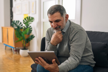 senior adult man sitting on sofa and using digital tablet at his home