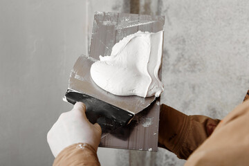 Construction worker with trowel and putty knife plastering a wall. House renovation concept. 