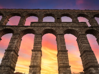 Bello atardecer en tonos anaranjados y azules, visto a través de los arcos del acueducto romano de Segovia, en Castilla y León,España - obrazy, fototapety, plakaty