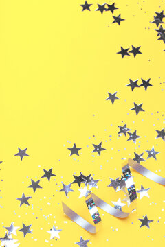 Shiny party streamers and stars on the trendy yellow background. Copy space. The concept of celebrations, the Day of St. Valentine, Christmas, New Year, birthday, etc.