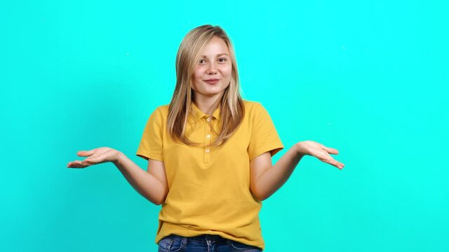 The young woman says wow, she smiles happily at the room. Beautiful Caucasian woman in yellow t-shirt and long blond hair standing on blue background. A fat teenager. Advertising concept.