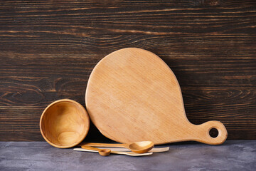 Wooden cutting board and kitchen utensils on a wooden background, space for text.