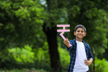 Cute indian little child holding indian rupees symbol in hand and showing expression