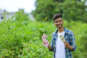 Naklejka na ściany i meble Young indian man holding dollar symbol in hand over nature background