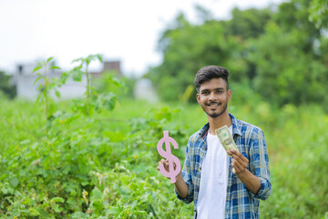 Young indian man holding dollar symbol in hand over nature background