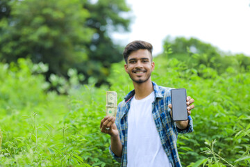 Young indian man holding dollar symbol in hand over nature background