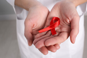 Woman holding red awareness ribbon indoors, closeup. World AIDS disease day