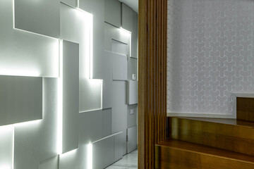 Modern hi-tech geometric design of wall with lamps in luxury interior. Wooden staircase.