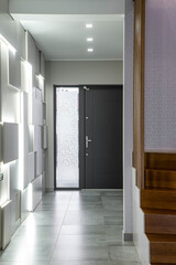 Contemporary interior of hall in luxury apartment. Modern design of wall. Iron door. Wooden staircase.