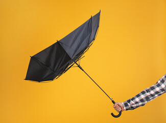 Man holding umbrella caught in gust of wind on yellow background, closeup