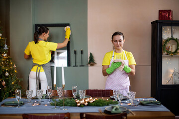 General cleaning before the winter holidays Christmas and New Year. Professional housekeeping service. Cleaning lady in yellow uniform and gloves cleans the room