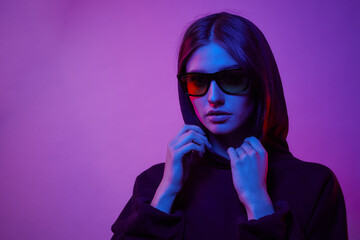 Girl posing in a studio in a trendy neon light. Woman in sunglasses and hoodie with colorful light effects.