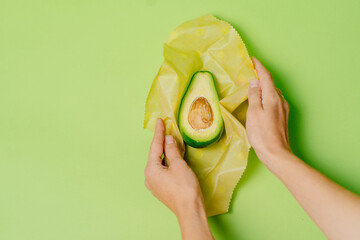 Organic fabric covers for food storage. Unrecognizable woman's hands holds reusable Beeswax Food Wraps with half of avocado.