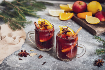 Two cups of mulled wine with spices, on the table. On the background of fruits and Christmas tree branches