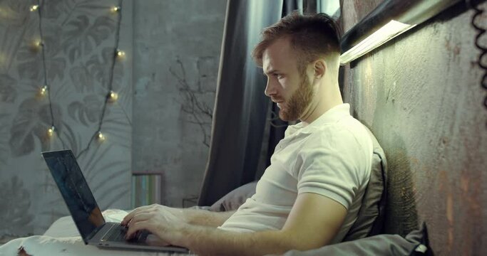 a man with a laptop in his bed in his bedroom. Slow motion.