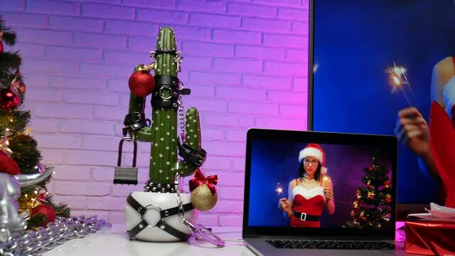 cactus dressed up in accessories for BDSM games on the Christmas table with gifts next to the TV with the image of a girl in a Santa Claus hat