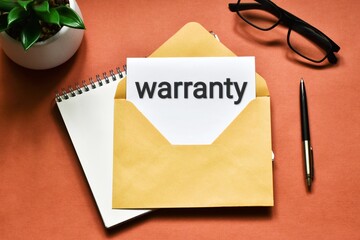 Warranty. Glasses, green plant a next to a envelope that says WARRANTY on a pink table. Flat lay. Business and finance concept.