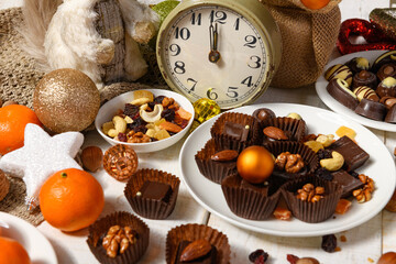 sweet food background for christmas or holiday decoration - chocolate candies, tangerines, nuts and dried fruits on white wood