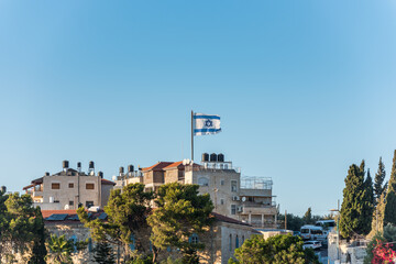 Israeli National flag waving on the top of Mount of Olive with background of residential houses in Jerusalem, Israel