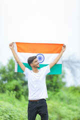 Young indian man waving indian national flag over nature background