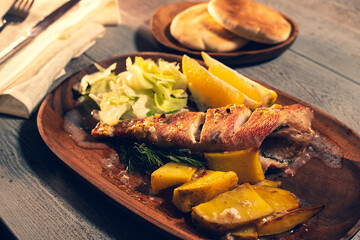 Red sea bass baked close up. Serving on a wood dish with baked potato and lemon. Rustic wood background. Seafood composition