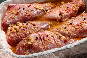 Close up of raw fish fillet of red perch prepared for baking with spices on a wood table background. Side view,  seafood cooking composition