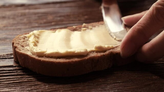 Close-up butter spreading on rustic rye bread with metal knife on wooden table