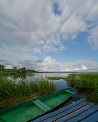 Green boat at the pier of the lake. Green grass, blue sky summer landscape 
