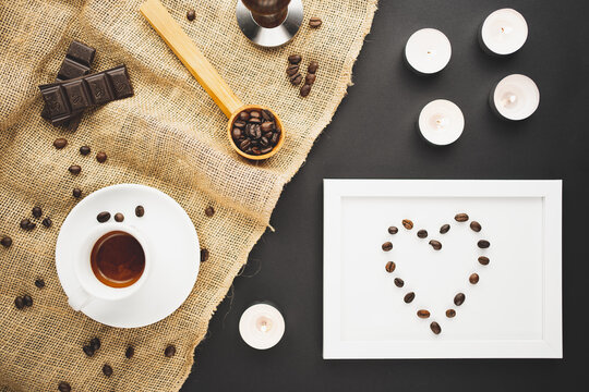 A cup of coffee espresso, chocolate, coffee beans and a picture frame with a heart and candles. Flat lay overhead shot.