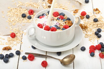 Oatmeal with raspberries, blueberries, nuts on a white wooden background