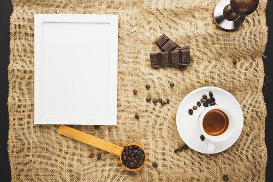 A cup full of espresso with chocolate and coffee beans and candles and a picture frame. Flat lay overhead shot.