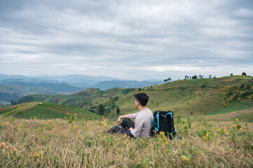 Fototapeta na wymiar Asian man relaxing with camera bag on farmland hill in rural