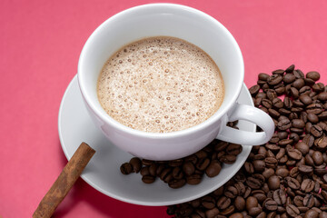 cup with cappuccino some roasted coffee beans and cinnamon stick, isolated on pink background